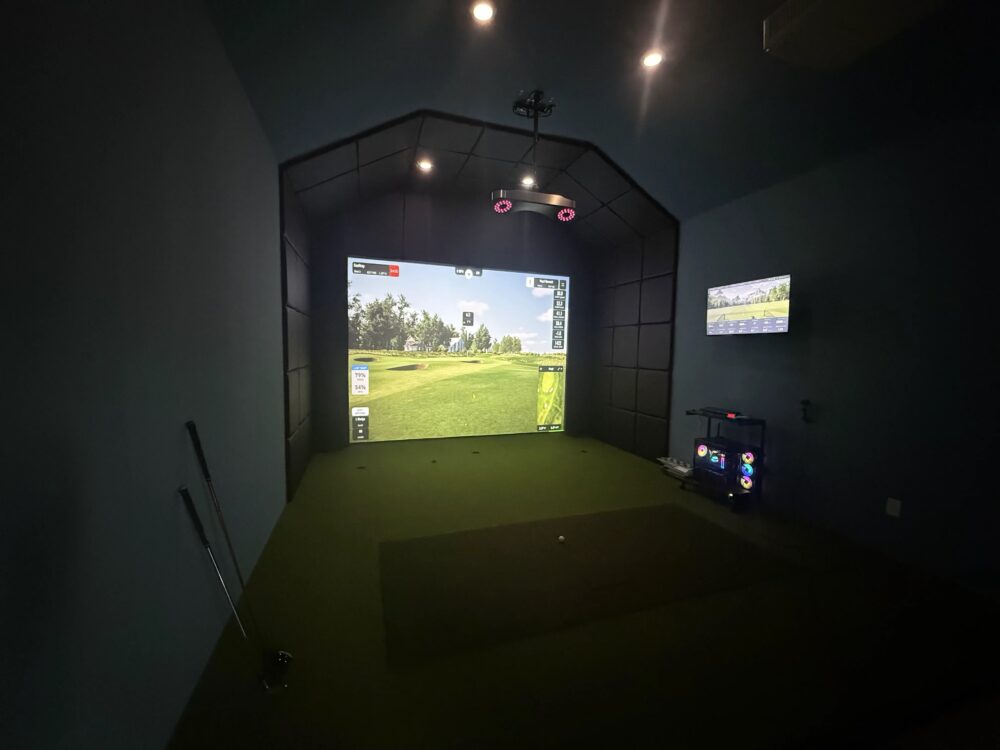 Custom home golf simulator in a navy media room with black padded enclosure and overhead launch monitor