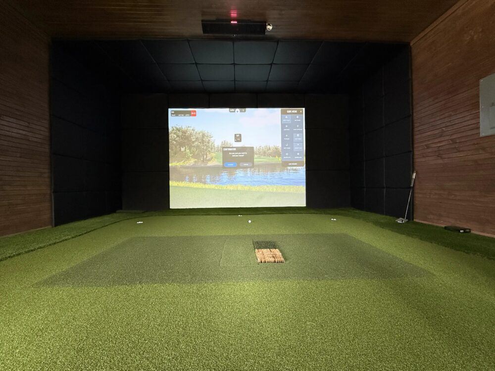 Wood-paneled home golf simulator room with wide turf hitting bay and ceiling-mounted launch monitor