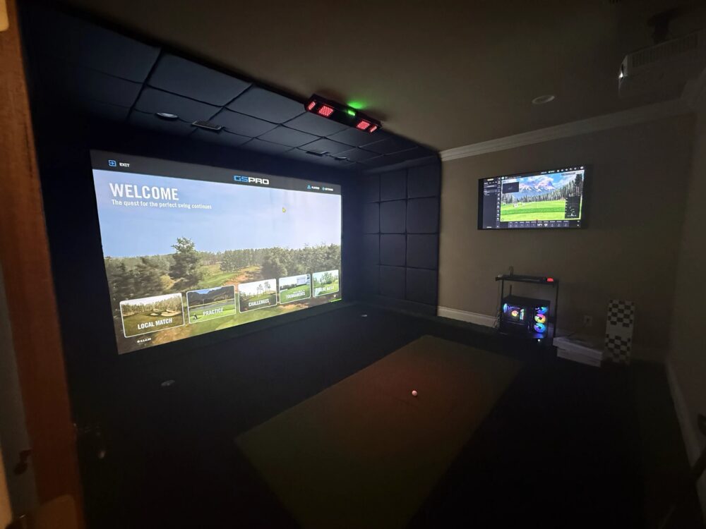 Home golf simulator running GSPro on a wide impact screen with side monitor and gaming PC